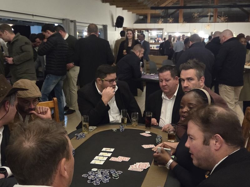 Poker players seated at a busy fun casino night with guests watching