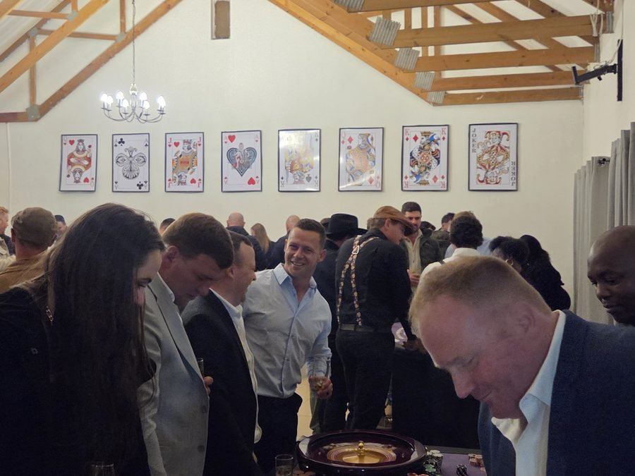 Guests gathered around a roulette wheel at a fun casino night in a hall decorated with playing cards